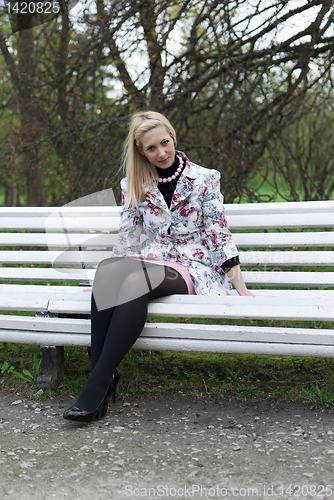Image of blonde girl sitting on a park bench 