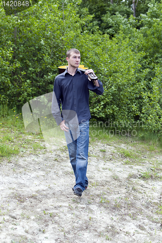 Image of man walks through the woods with his guitar