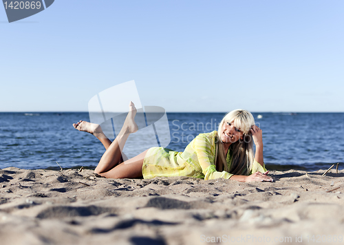 Image of blonde girl in a yellow tunic lies near the sea on his knees