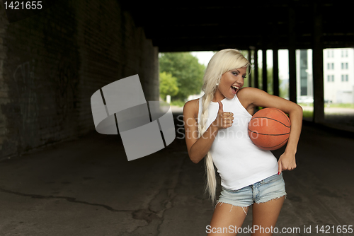 Image of beautiful smiling girl standing with a basketball in the street, thumbs up