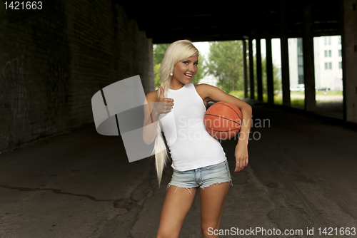 Image of beautiful smiling girl standing with a basketball in the street, thumbs up