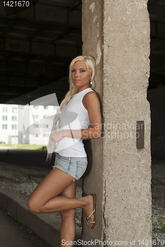 Image of athletic girl in denim shorts and white T-shirt standing at the pillar