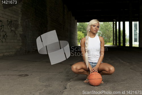 Image of Beautiful blonde girl is sitting with basketball on the street