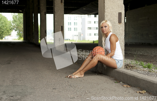 Image of Beautiful blonde girl is sitting with basketball on the street