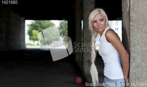 Image of athletic girl in denim shorts and white T-shirt standing at the pillar