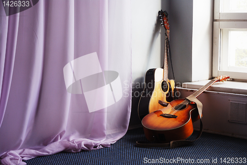 Image of two acoustic guitar next the window