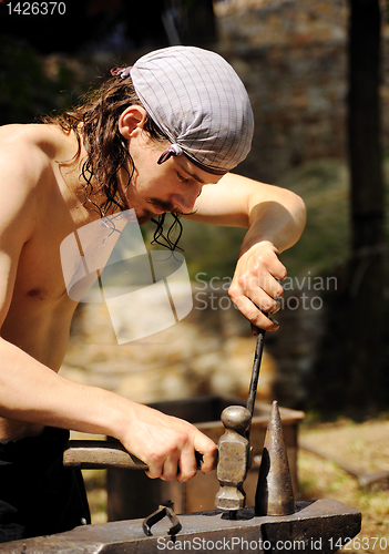 Image of Young blacksmith hammering hot iron on anvil