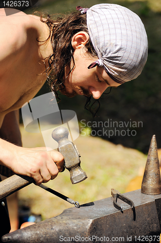 Image of Young blacksmith hammering hot iron on anvil