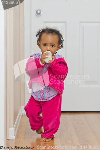 Image of A cute baby girl walking with her bottle