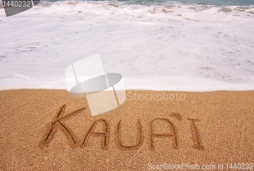 Image of The word Kauai written into the sand in front of surging tide