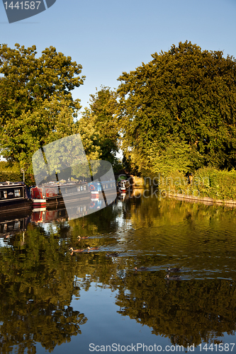 Image of Canal barges reflected in calm water disturbed by ducks