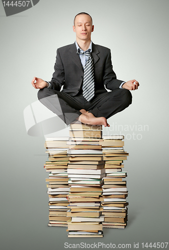 Image of businessman in lotus pose with many books near