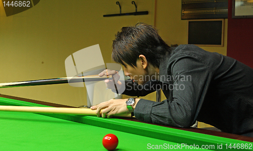 Image of Young man concentrating while aiming at pool ball while playing 