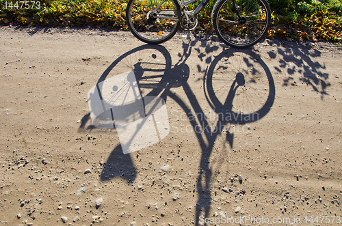 Image of Standing bicycle shadow on gravel road.