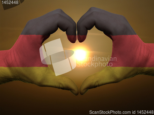 Image of Heart and love gesture by hands colored in germany flag during b