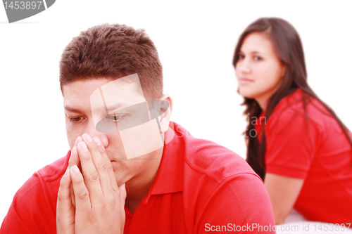 Image of Young sad man sitting on bed, nearby unsatisfied woman. 