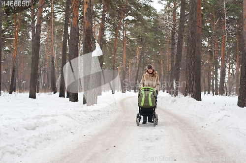 Image of Young mother with baby carriage in winter forest