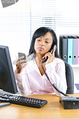 Image of Black businesswoman using two phones at desk