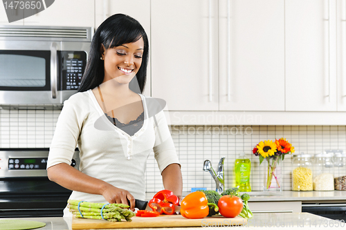 Image of Young woman cutting vegetables in kitchen