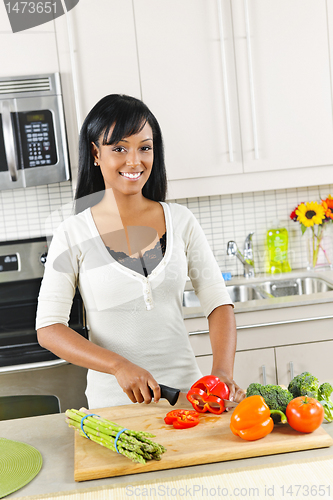 Image of Young woman cutting vegetables in kitchen