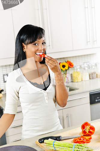 Image of Young woman tasting vegetables in kitchen