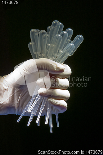 Image of Hand in white gloves holding many pipettes