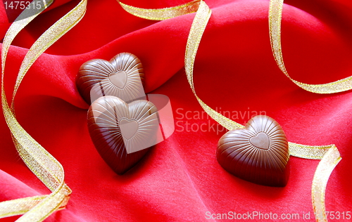 Image of Chocolate hearts and gold ribbon on a red background.