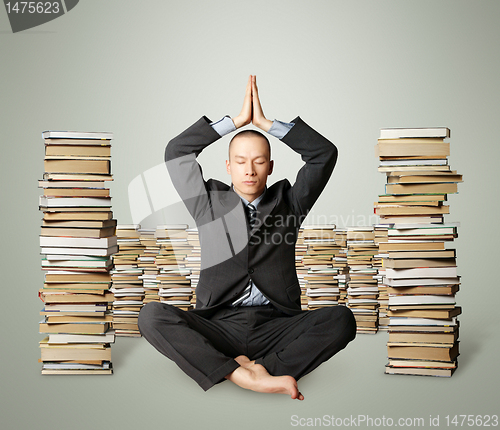 Image of businessman in lotus pose with many books near