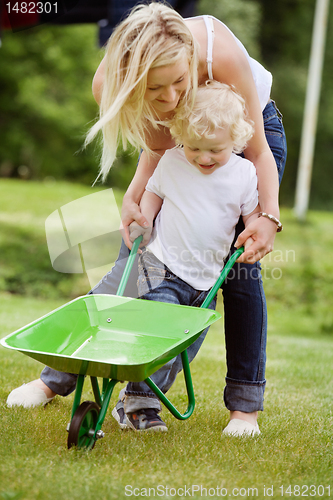 Image of Mother helping her kid in pushing wheelbarrow