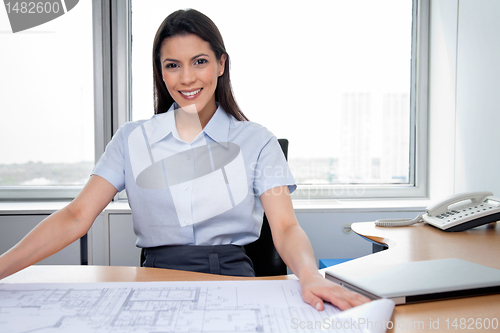 Image of Female Architect Sitting With Blueprints On Desk