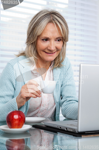 Image of Woman Working on Laptop While Having Cup of Tea