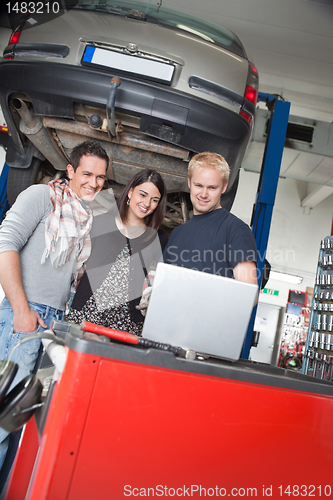 Image of Couple standing with mechanic using laptop