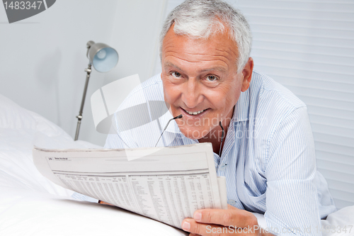 Image of Man Reading Newspaper on Bed