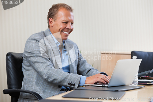 Image of Cheerful businessman working on laptop