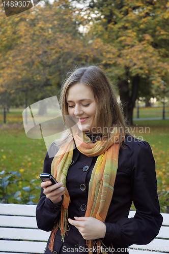 Image of woman reads the message on phone in autumn park