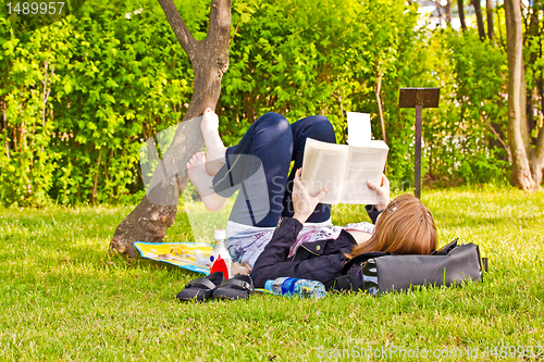 Image of Young girl with a book lying on a lawn in a park