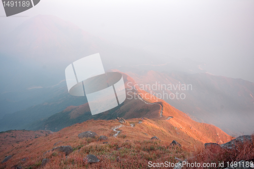 Image of dark landscape with fog between hills and orange sky before sunr