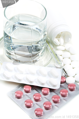 Image of Different pills, glass of water and medical thermometer.