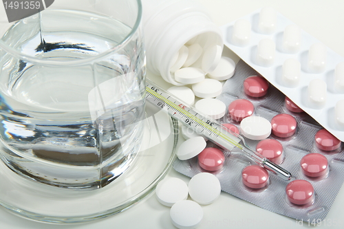 Image of Different pills, glass of water and medical thermometer.