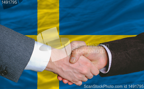 Image of businessmen handshake after good deal in front of sweden flag