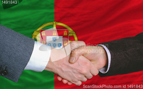 Image of businessmen handshake after good deal in front of portugal flag