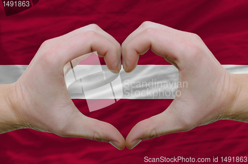 Image of Heart and love gesture showed by hands over flag of latvia backg