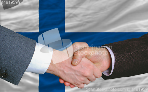 Image of businessmen handshake after good deal in front of finland flag