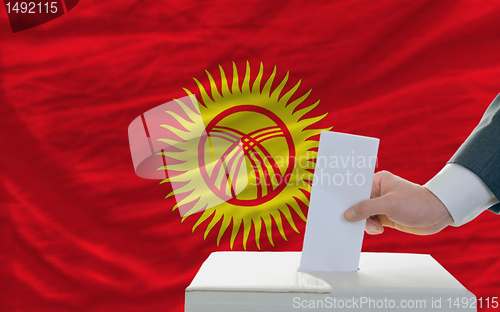 Image of man voting on elections in kyrghyzstan in front of flag