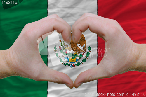 Image of Heart and love gesture showed by hands over flag of mexico backg