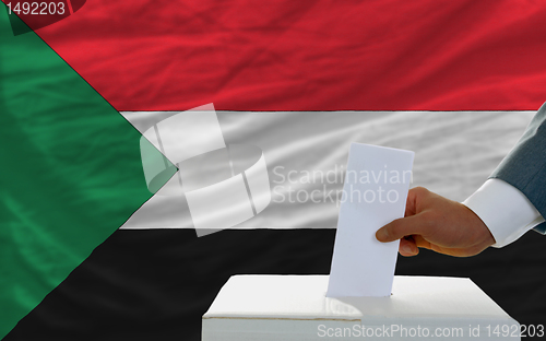 Image of man voting on elections in sudan in front of flag