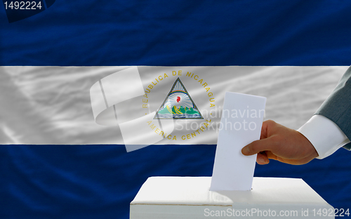 Image of man voting on elections in nicaragua in front of flag