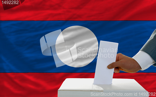 Image of man voting on elections in laos in front of flag