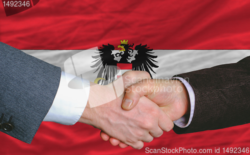 Image of businessmen handshake after good deal in front of austria flag