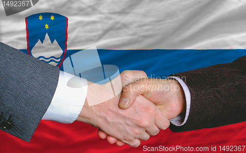 Image of businessmen handshake after good deal in front of slovenia flag